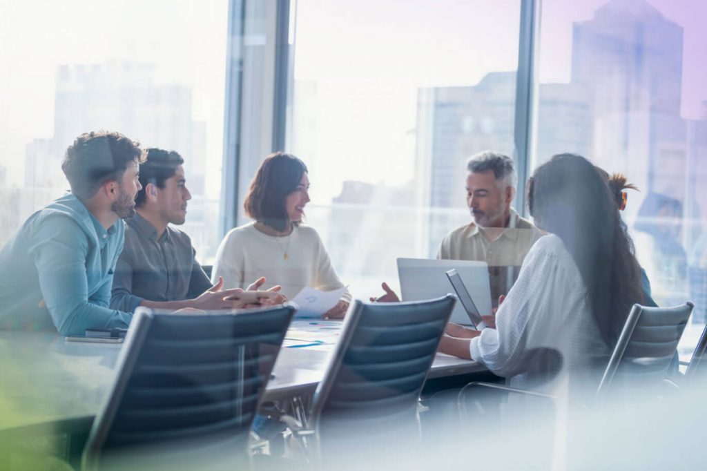 Looking into a conference room of five people sitting at a table discussing financial solutions.