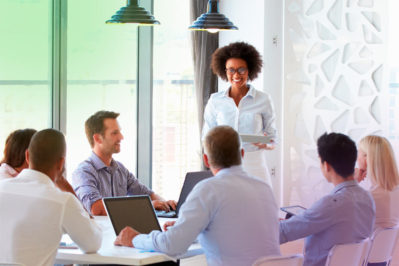 A woman standing in front of a group of business professionals seated at a table, likely discussing dividend services, dividend payment, and dividend-driven strategies.